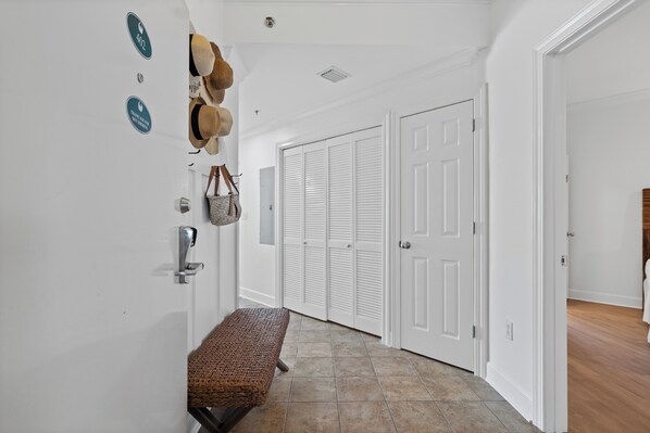 A hallway with a bench, white doors, and a wall with hats and a hanging bag. - Phoenix IX 402 | Walk to Flora Bama! | Pools, Hot Tub & Much More! | My Beach Getaways (Orange Beach)