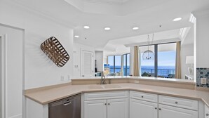 Una cocina moderna con armarios blancos, lavavajillas y un amplio ventanal con vista al océano.