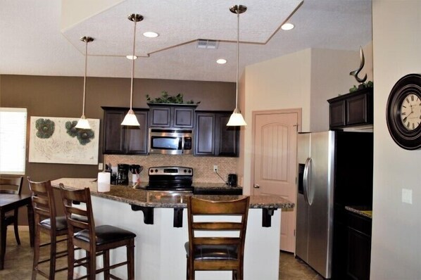 A modern kitchen with dark cabinets, stainless steel appliances, and pendant lighting.