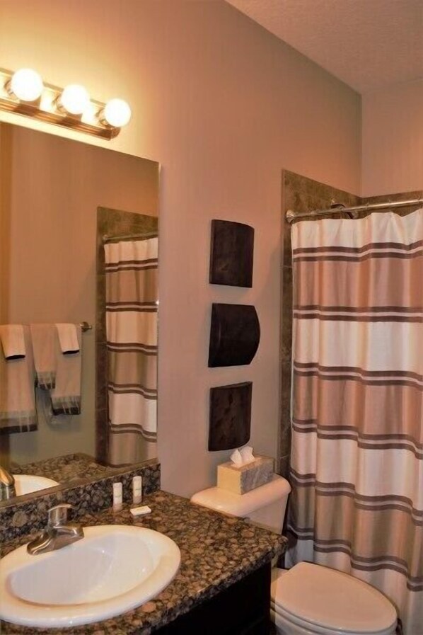 A bathroom with a granite countertop sink, a mirror with lights, a toilet, and a striped shower curtain. - Fairway Haven Retreat by Mesquite Vacation Rentals with Putting Green and $510 in free daily activities (Mesquite)