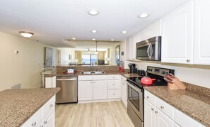 A modern kitchen with white cabinets, granite countertops, stainless steel appliances, and a view of the ocean.