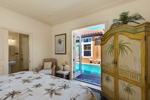 A bedroom with a bed, a chair, a nightstand, a lamp, and a view of a swimming pool.