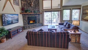 A cozy living room with a stone fireplace, a large flat-screen TV, a striped sofa, and a coffee table. - Spacious Townhome Mountain View & Private Hot Tub (Keystone)