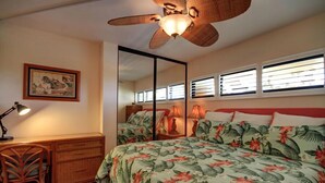 Une chambre à coucher comprenant un lit, un bureau, une chaise, un ventilateur de plafond et une fenêtre avec des stores.