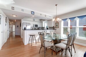 A modern kitchen with white cabinetry, a central island, and a dining area with a glass table and metal chairs. - Oceanfront Condo just steps to beach, pool, and main strip - Ocean Palms 201 (Isle of Palms)