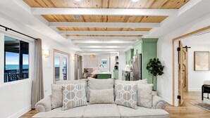 A modern living room with a beige sofa, wooden ceiling beams, and a view to a balcony. - Gulf Front | Pet Friendly | Spacious Porch (Gulf Shores)