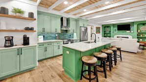 A modern kitchen with green cabinets, a large island with stools, and a wooden ceiling. - Gulf Front | Pet Friendly | Spacious Porch (Gulf Shores)