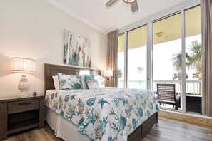 Quarto com uma cama grande, uma mesa de cabeceira, um ventilador de teto e vista para o exterior por uma porta de vidro deslizante.