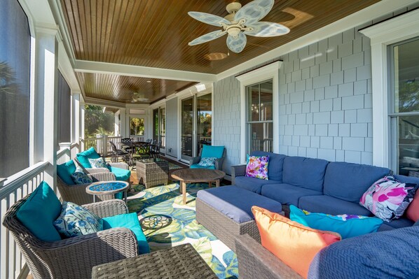 A covered outdoor seating area with wicker furniture, a blue sofa, and a ceiling fan. - Stunning Home! Pool, Theater Room, Steps to Beach - 3 46th Avenue (Isle Of Palms)