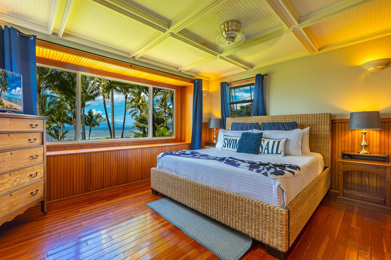 A bedroom with a large window offering a view of palm trees and the ocean.