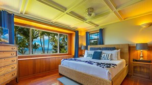 A bedroom with a large window offering a view of palm trees and the ocean.