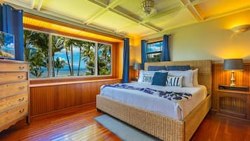 A bedroom with a large window offering a view of palm trees and the ocean.
