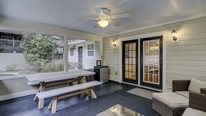 Un patio couvert avec une table et des bancs, un ventilateur de plafond et une porte à panneaux de verre.