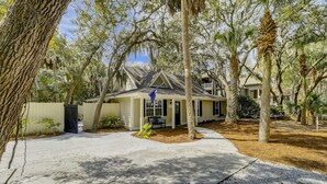 Une maison de plain-pied dotée d’un porche à l’avant, entourée d’arbres matures et d’une pelouse bien entretenue.