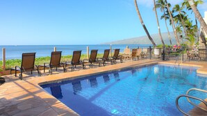 A poolside area with lounge chairs and palm trees, overlooking a body of water.