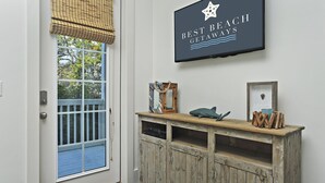 Ein Zimmer mit weißer Tür, einem Fenster mit Blick auf ein blaues Deck, einem an der Wand befestigten Schild mit der Aufschrift 'Best Beach Getaways' und einem rustikalen Holztischchen mit Dekoration.
