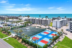 A hotel with multiple floors, a tennis court, and a view of the ocean.