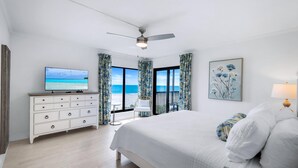 A bedroom with a bed, a TV, a dresser, a ceiling fan, and a view of the ocean.