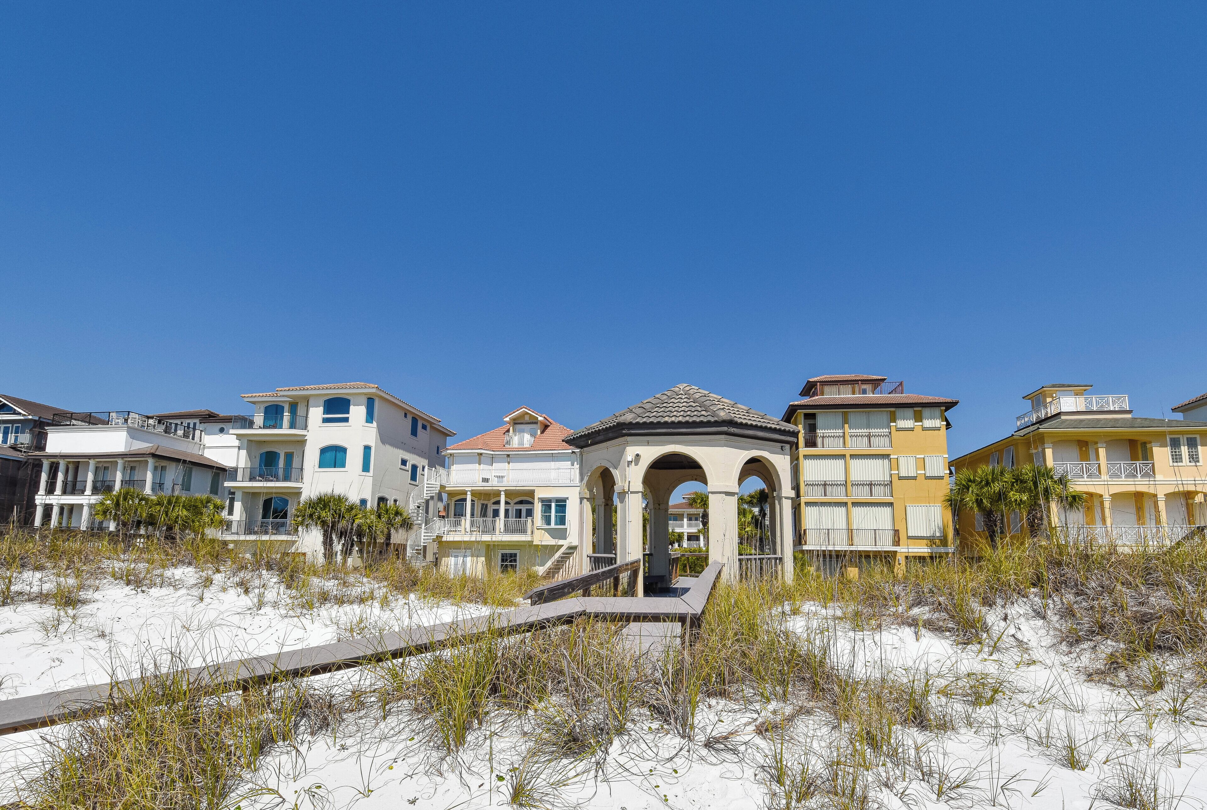 A beachfront property with a gazebo, sandy beach, and multi-story buildings.