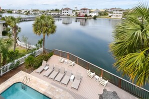 A pool area with lounge chairs and a small pool, surrounded by a white fence and palm trees, overlooking a calm body of water and residential buildings. - Luxury Lakefront Home w/ Beach Service & Private Pool in Dunes of Destin! 🌊☀ (Destin)