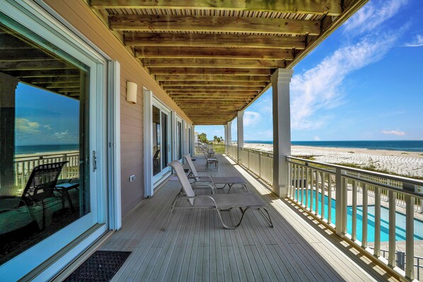 Relax on the deck with a view of the beach, surrounded by lounge chairs and a table.