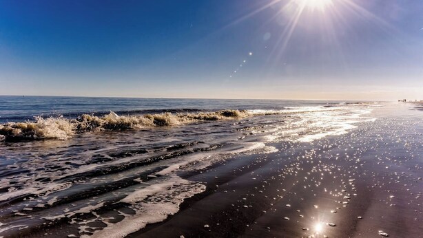 Ein Strand mit Wellen, blauem Himmel und strahlender Sonne.