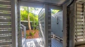 Une porte ouverte donne sur un espace extérieur abrité, doté d’un toit en métal, d’une petite table et d’un banc.
