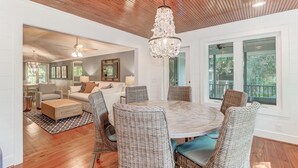 Un salon spacieux avec une table de salle à manger ronde entourée de chaises en osier, un lustre et un plafond en bois.