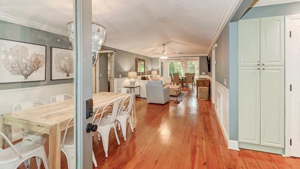 Une cuisine spacieuse avec un plancher en bois, un coin repas avec des chaises blanches et un mur bleu clair.