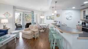 A modern kitchen with a bar area, dining set, and a view to the outside. - Condo at Baytowne! Large Balcony, Tropical Pool, Walk to Wharf, Tram to Beach (Miramar Beach)