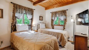A bedroom with two beds, wooden ceiling beams, large windows with curtains, a bedside lamp, and a TV stand. - Brookside: A Beautiful Chalet-Style Getaway on the Shore of Seneca Lake! (Dundee)
