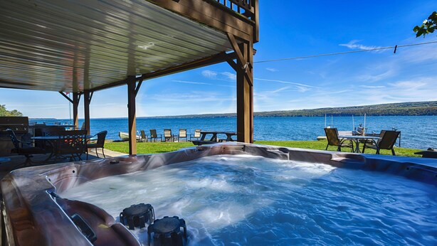 Un bain à remous avec vue sur un lac et des chaises sous une pergola en bois.