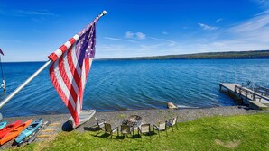 Un mât sur lequel flotte le drapeau américain, des kayaks, une jetée et un foyer au bord d’un lac.