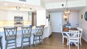 Une cuisine moderne avec des meubles blancs, un four à micro-ondes et une cuisinière. On y trouve également un coin repas avec une table en bois et des chaises blanches.
