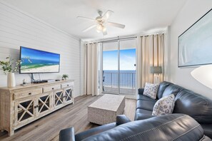 A living room with a flat-screen TV, leather sofa, wooden cabinet, and a balcony with a view. - Lighthouse 1107 by Liquid Life (Gulf Shores)