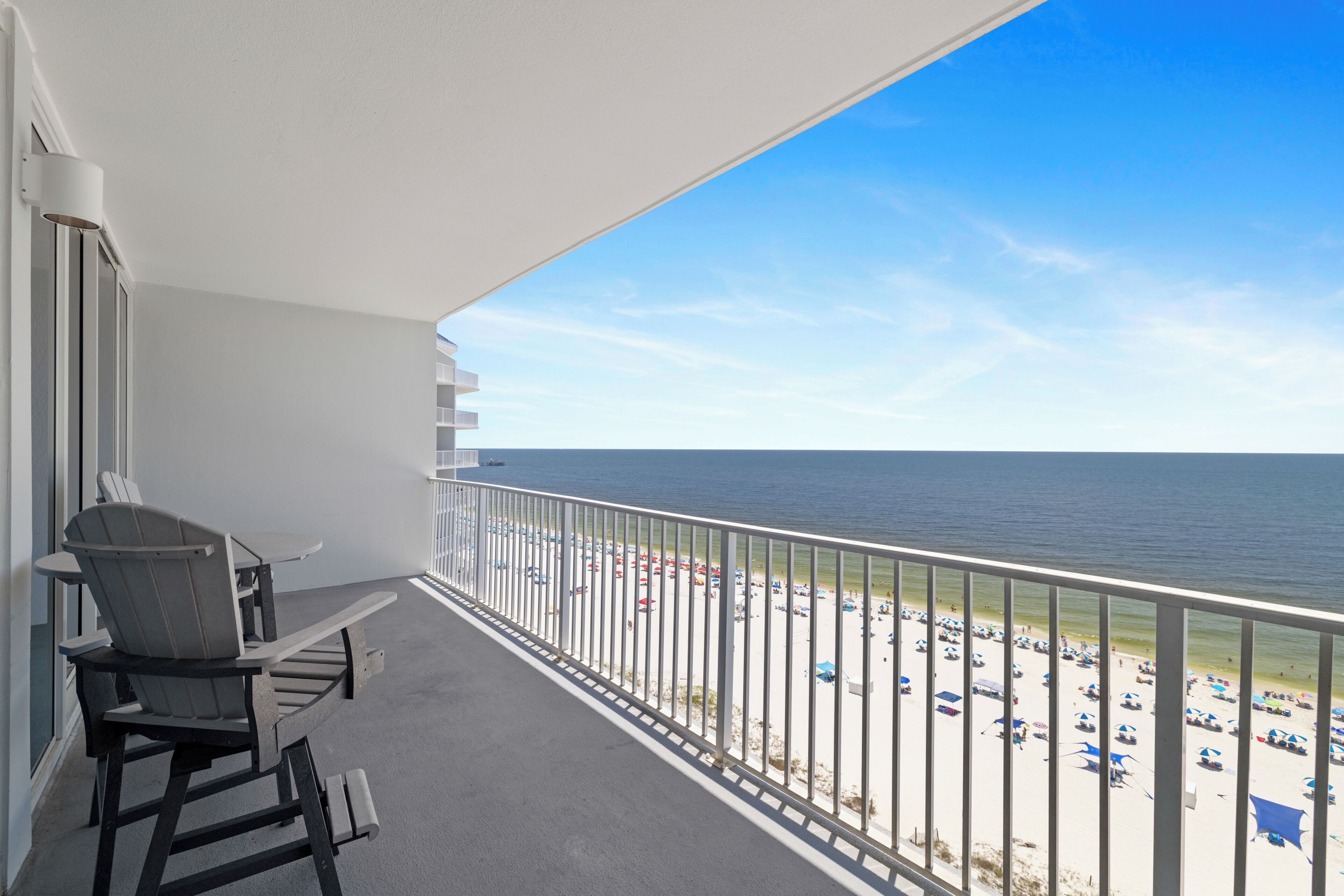 A balcony with a view of the beach, a table, and two chairs.