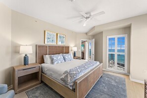 A bedroom with a bed, nightstands, a ceiling fan, and a view of the balcony.