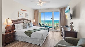 A hotel room with a bed, a nightstand, a lamp, a statue, a painting, and a view of the ocean.