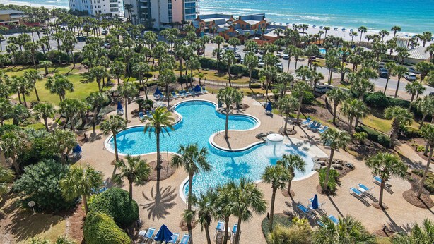 A resort with a large pool, palm trees, and a view of the ocean.
