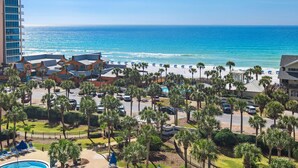 A hotel with a view of the ocean, palm trees, and a parking area.
