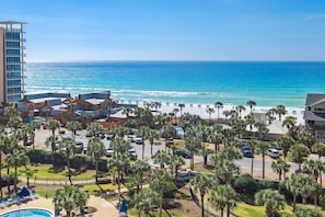 A hotel with a view of the ocean, palm trees, and a parking area.
