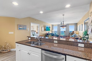 A kitchen with granite countertops, a dishwasher, and a view to the living area.