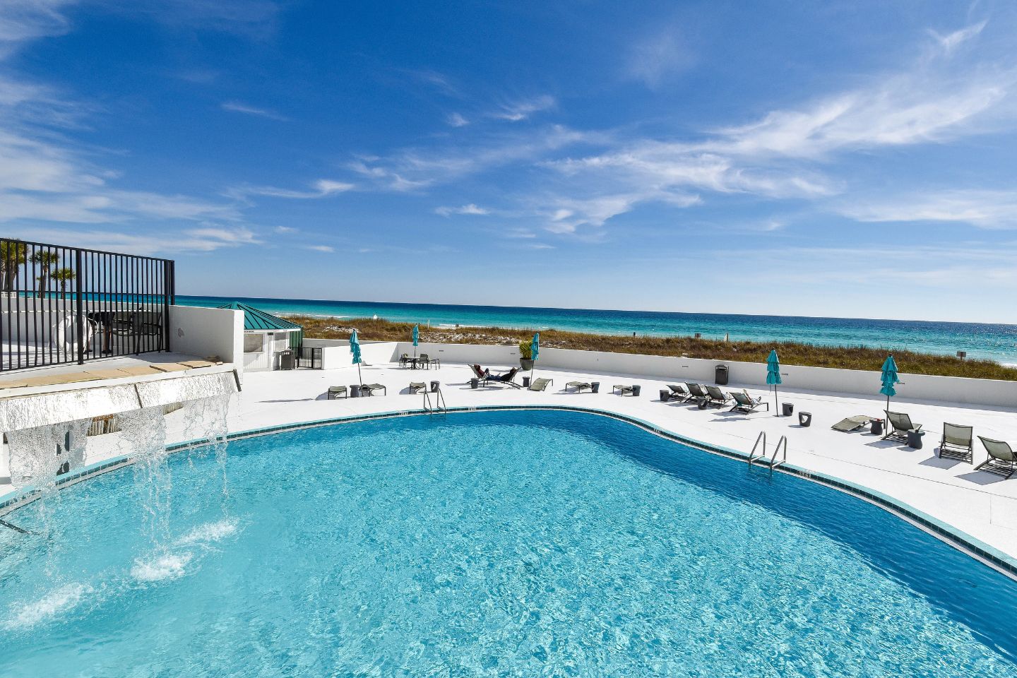 Ein Poolbereich mit Blick auf das Meer, Liegestühle und eine umzäunte Terrasse.