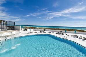 A pool area with a view of the ocean, lounge chairs, and a fenced deck.