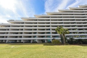 Un hotel de varios pisos con diseño de techo plano, balcones en cada planta y un césped bien cuidado en primer plano.