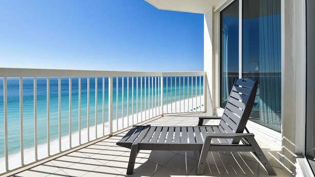 A balcony with a view of the ocean, a chair, and a glass door.