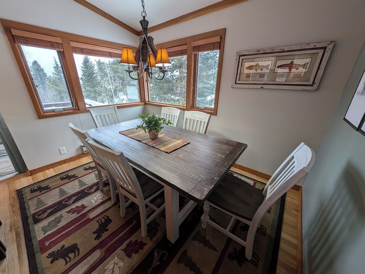 A dining area with a wooden table, white chairs, a chandelier, and a framed fish picture on the wall.