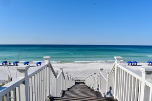 A wooden staircase leading to a beach with white railings and blue umbrellas.