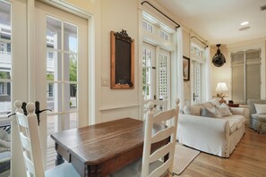 A living room with a wooden dining table, white chairs, a sofa, and a lamp.
