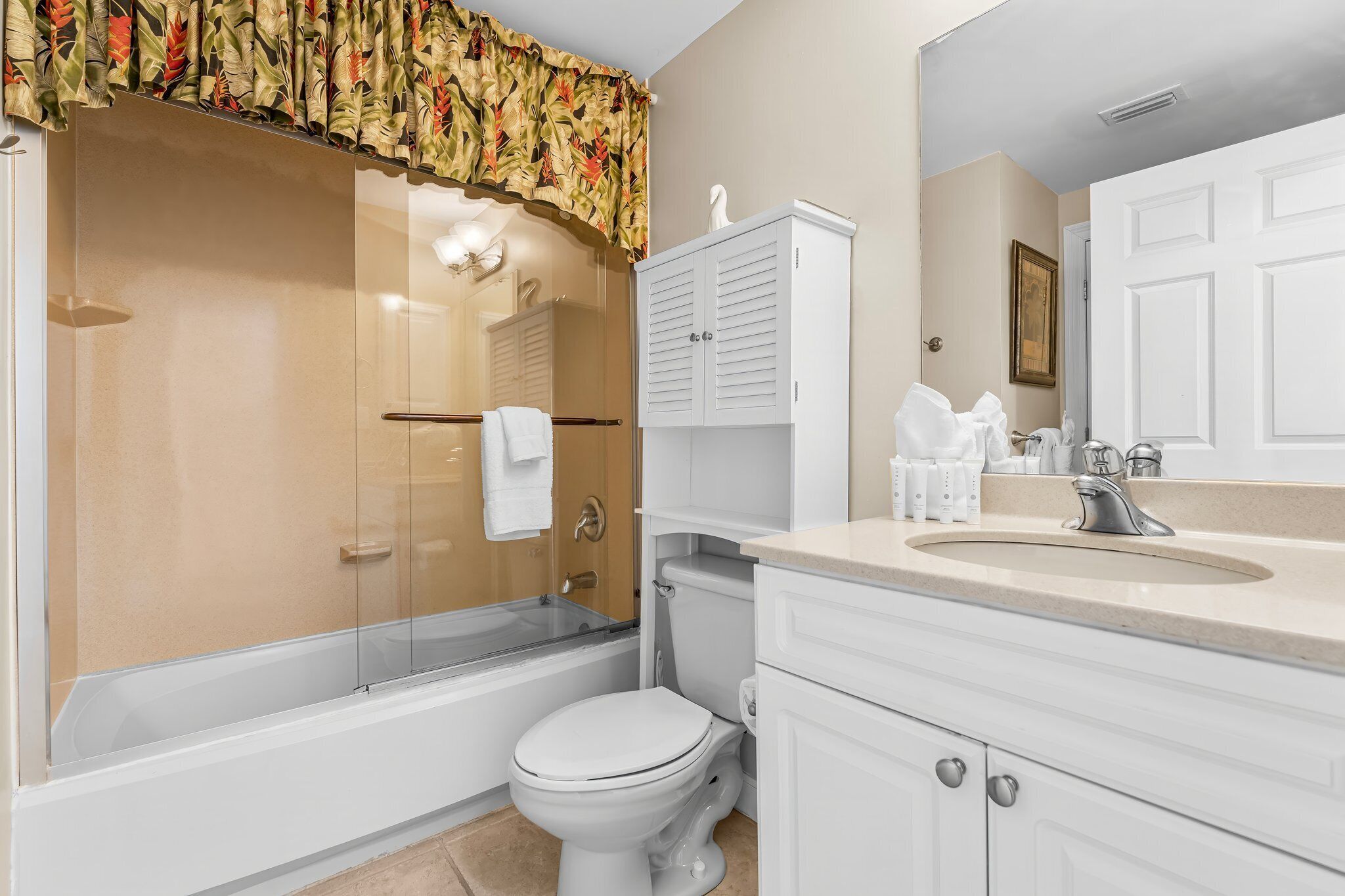 A bathroom with a glass-enclosed shower, a toilet, a sink with a mirror, and a cabinet.